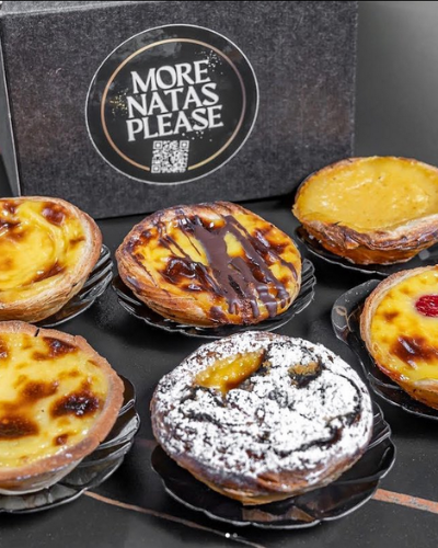 A collection of Portuguese Pastéis de Nata on display with 'More Natas Please' branding.